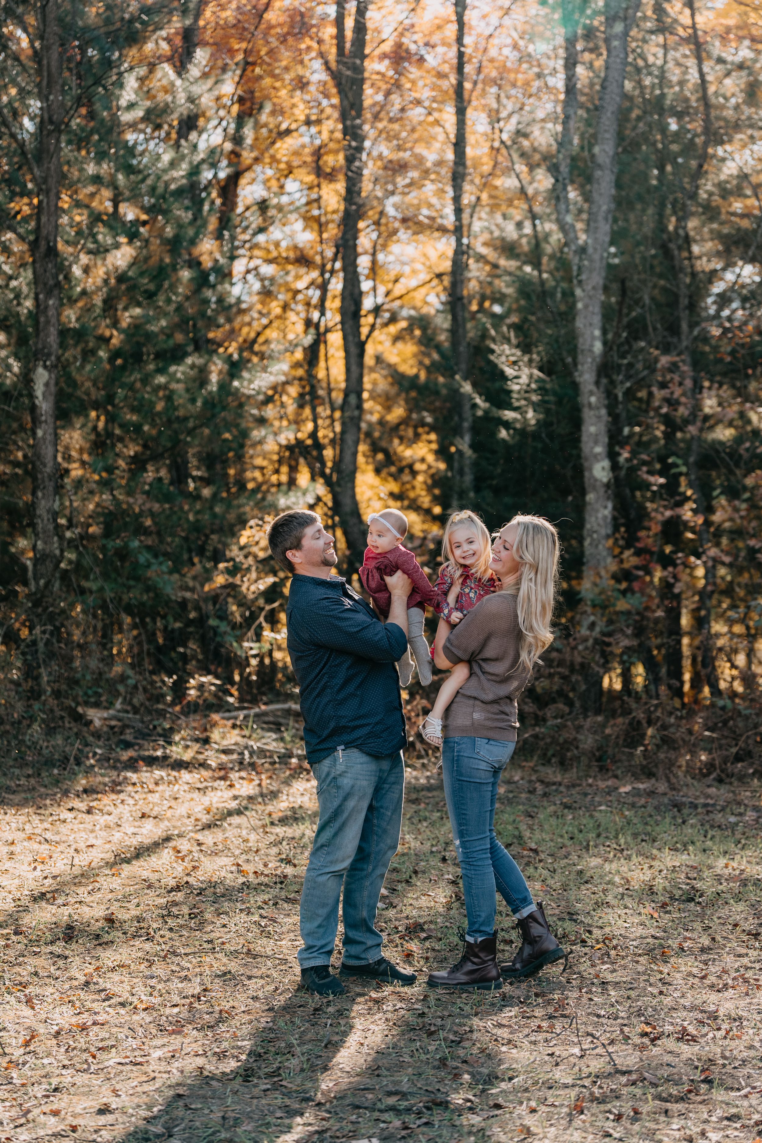 A candid moment between a group during a fall photoshoot with autumn trees in the background.