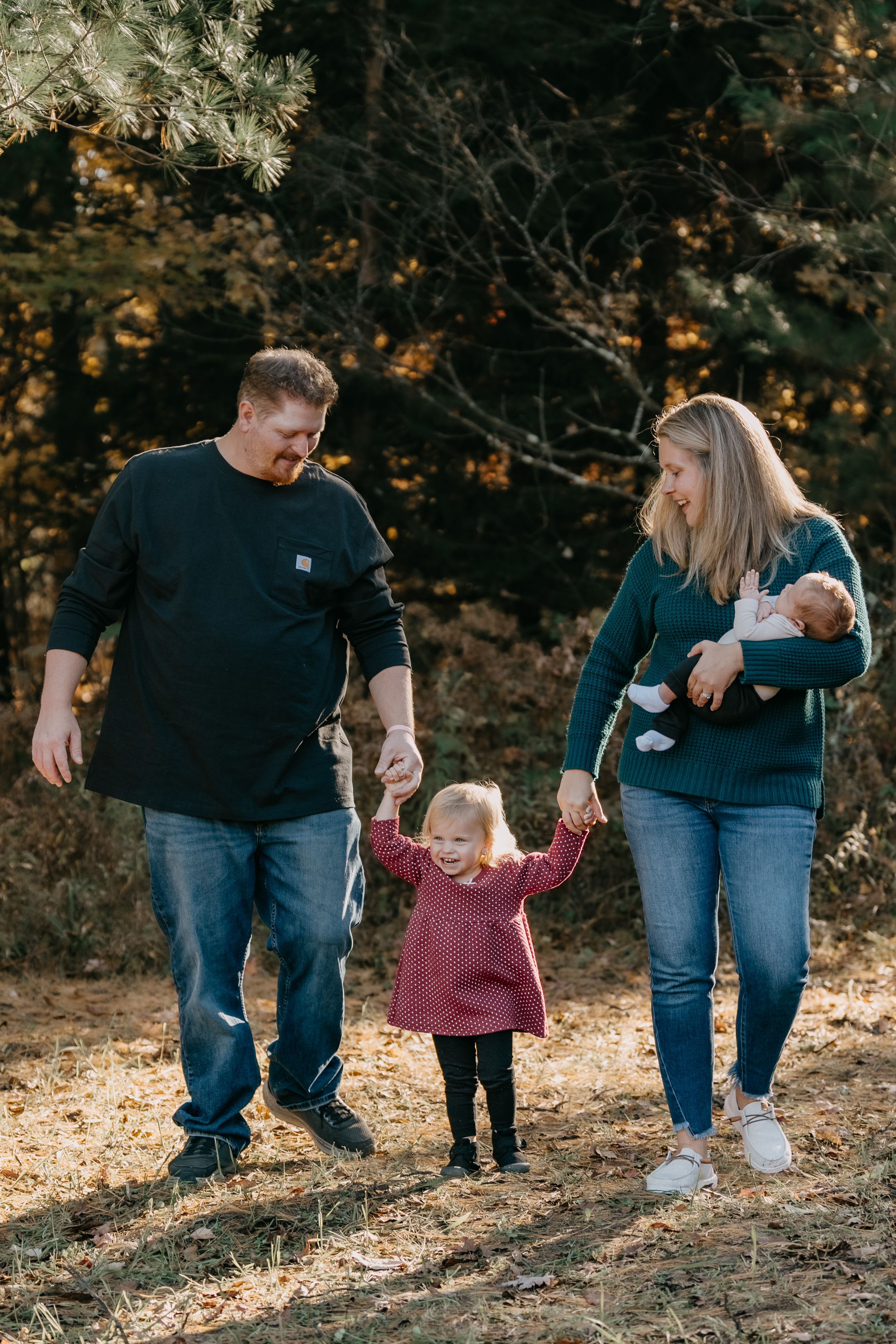 Family of four walks together on a wooded trail during golden hour autumn light.