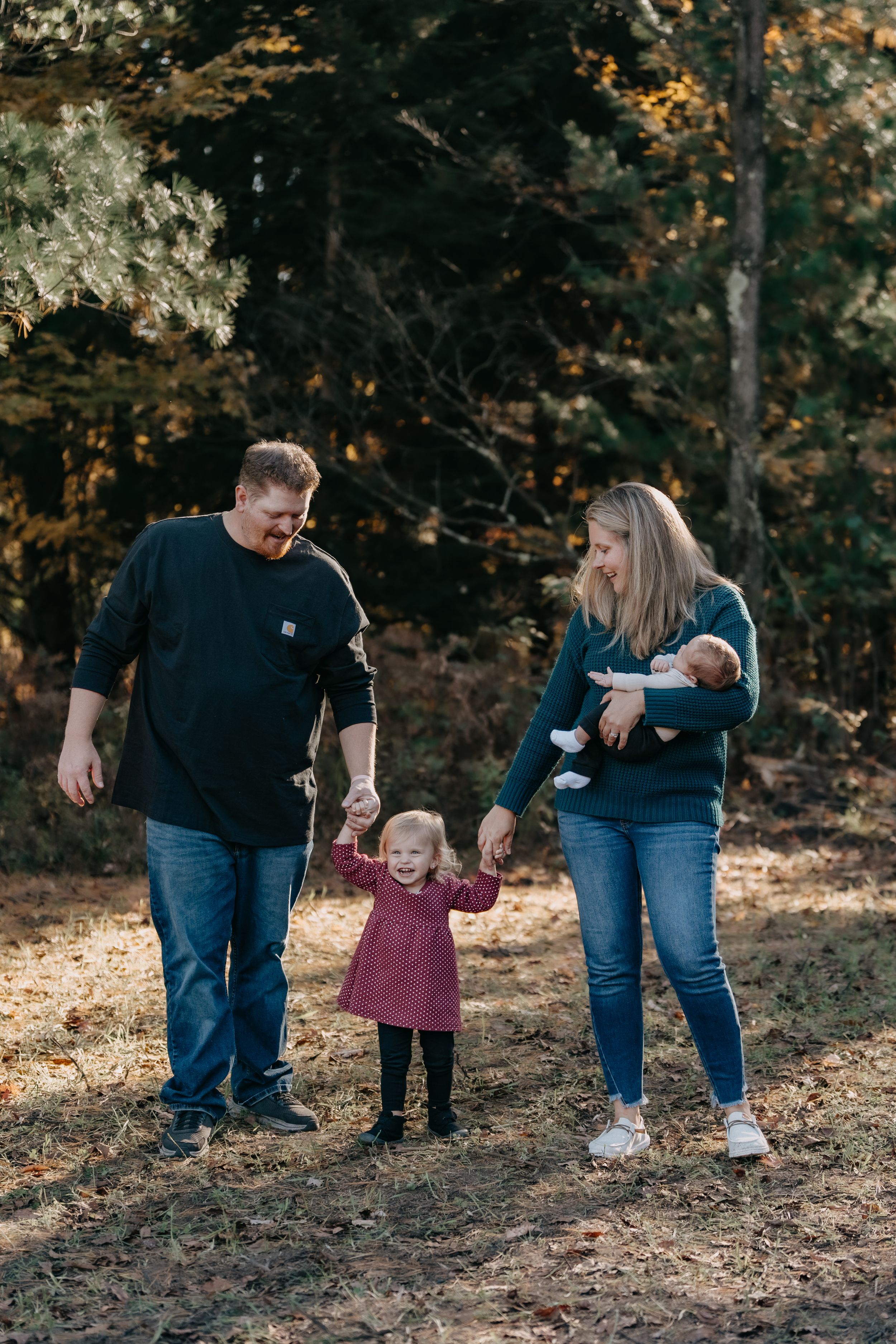 Family walking together and sharing a joyful moment in an autumn forest setting with fallen leaves.