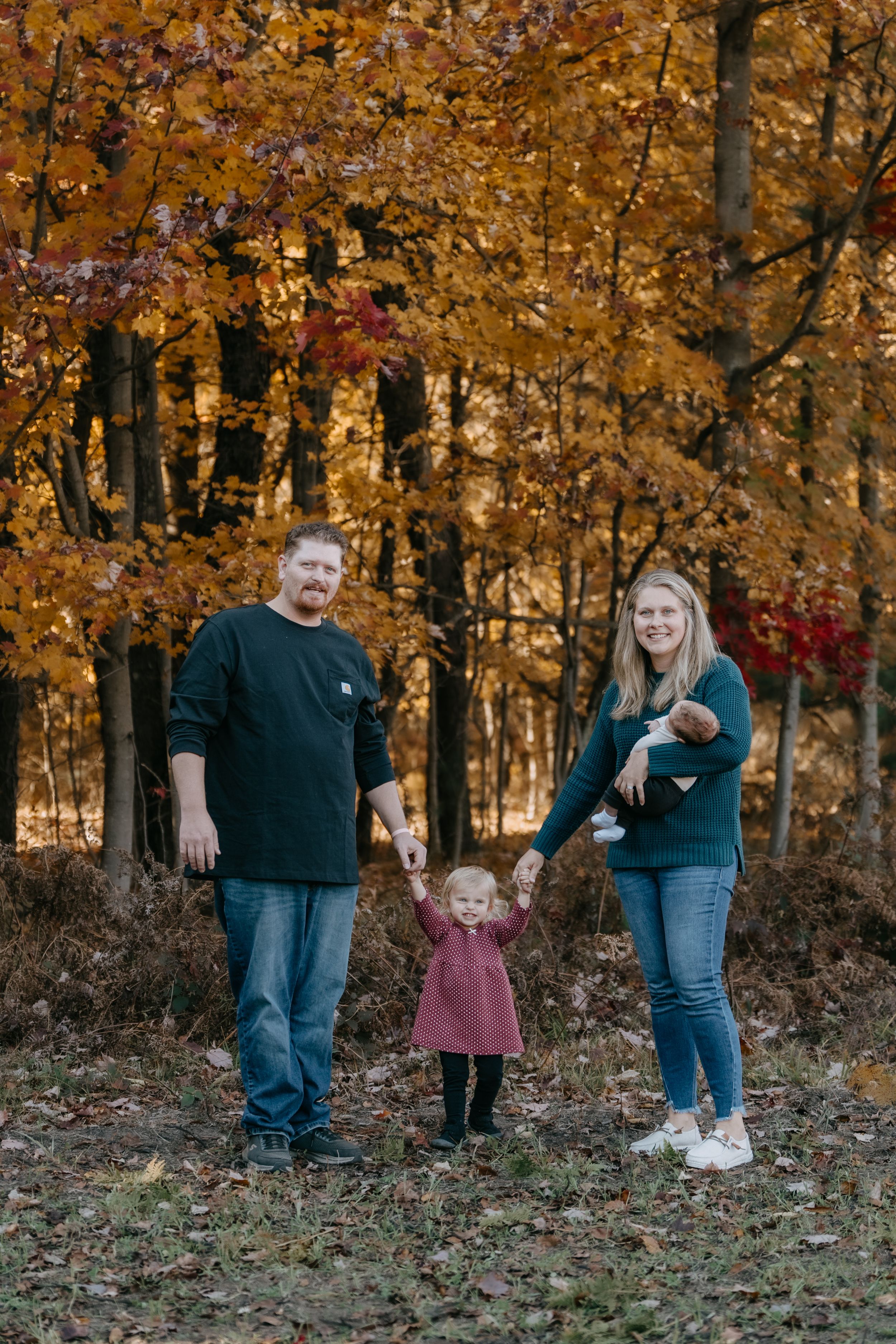 A family stands together in a wooded area with vibrant golden autumn foliage creating a warm seasonal backdrop.