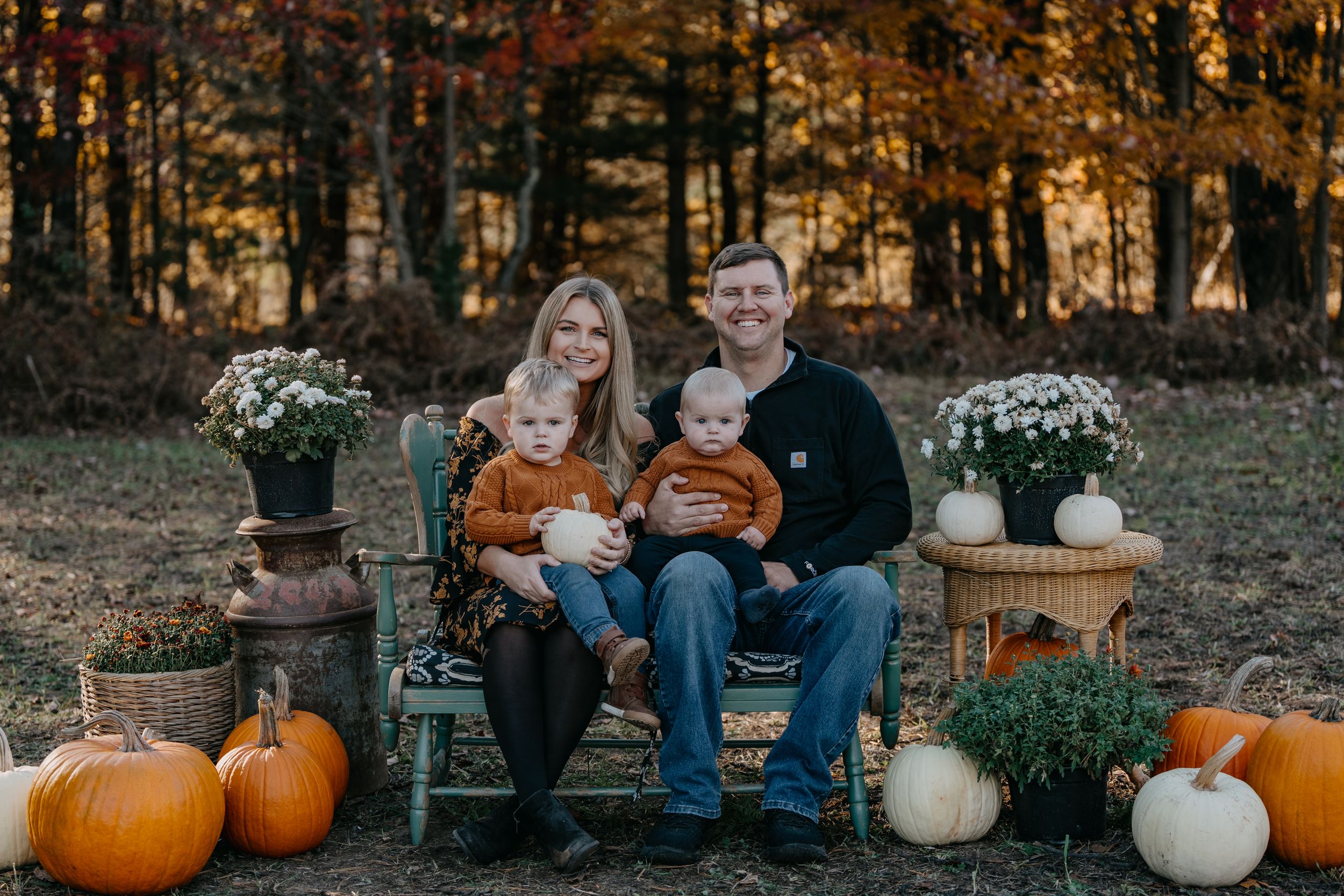 A fall photo session in a rustic outdoor setting with autumn pumpkins and white mums decorating the scene.