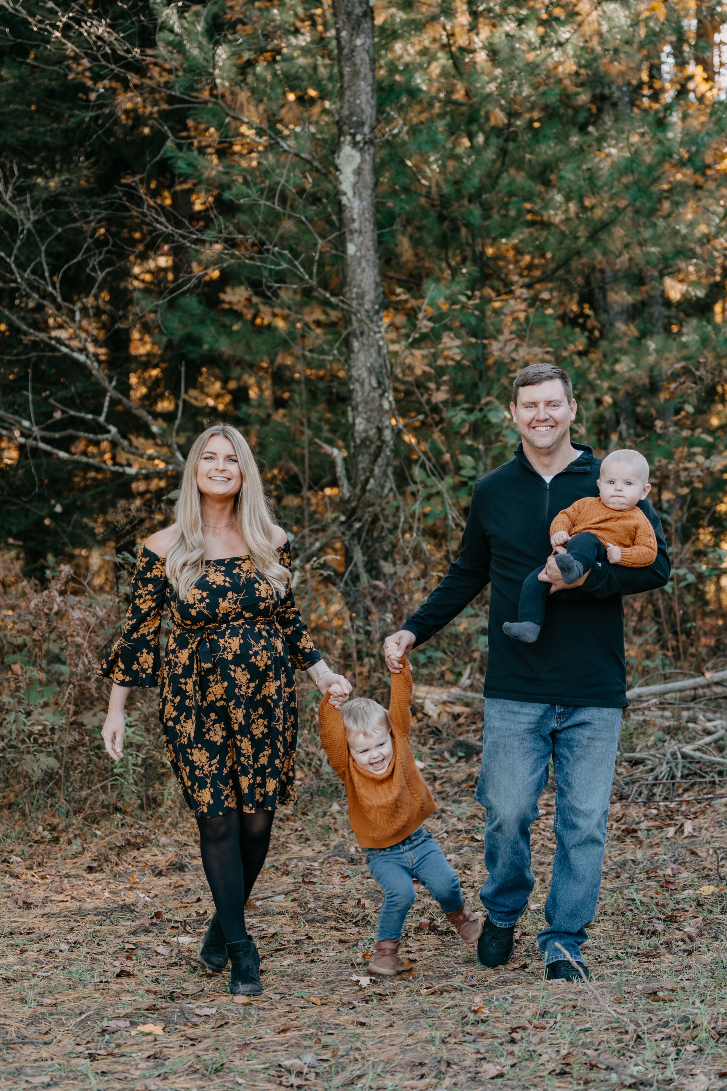 A family walks together on an autumn forest path surrounded by fall foliage and golden light.