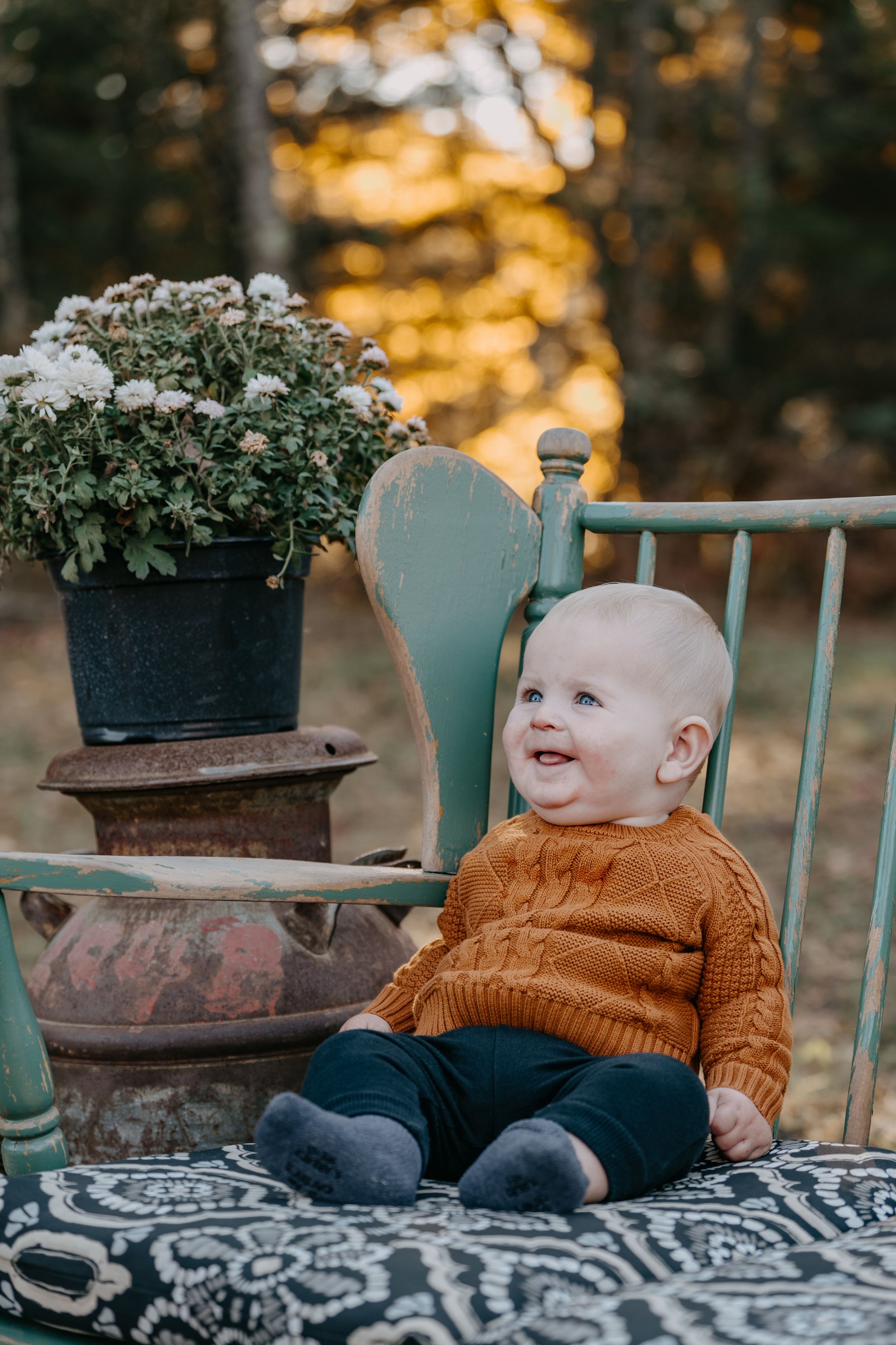 Small child wearing brown sweater sitting on outdoor patio with potted plants in golden sunset lighting.