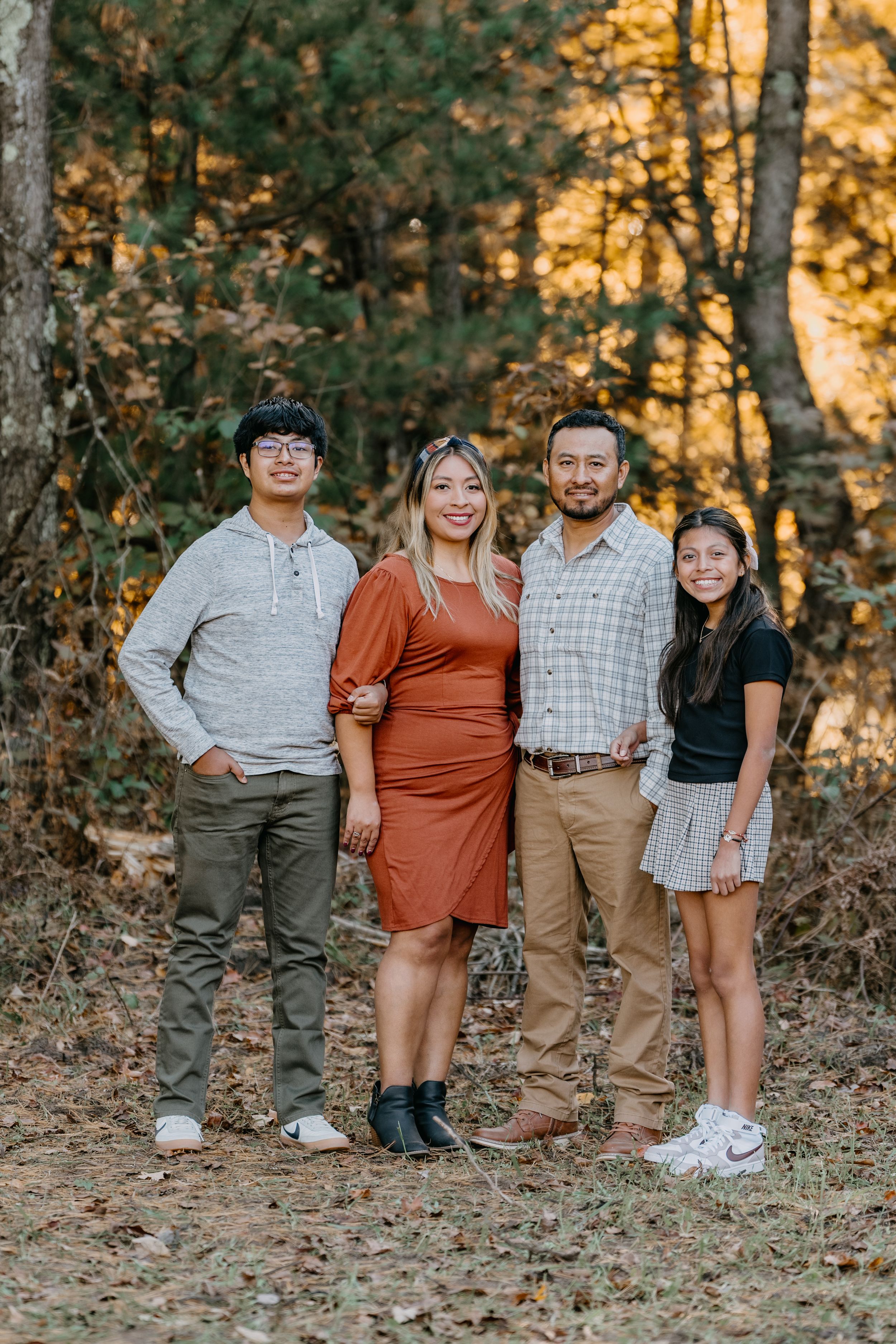 A group of people pose casually together outdoors in a wooded setting during golden hour sunset.