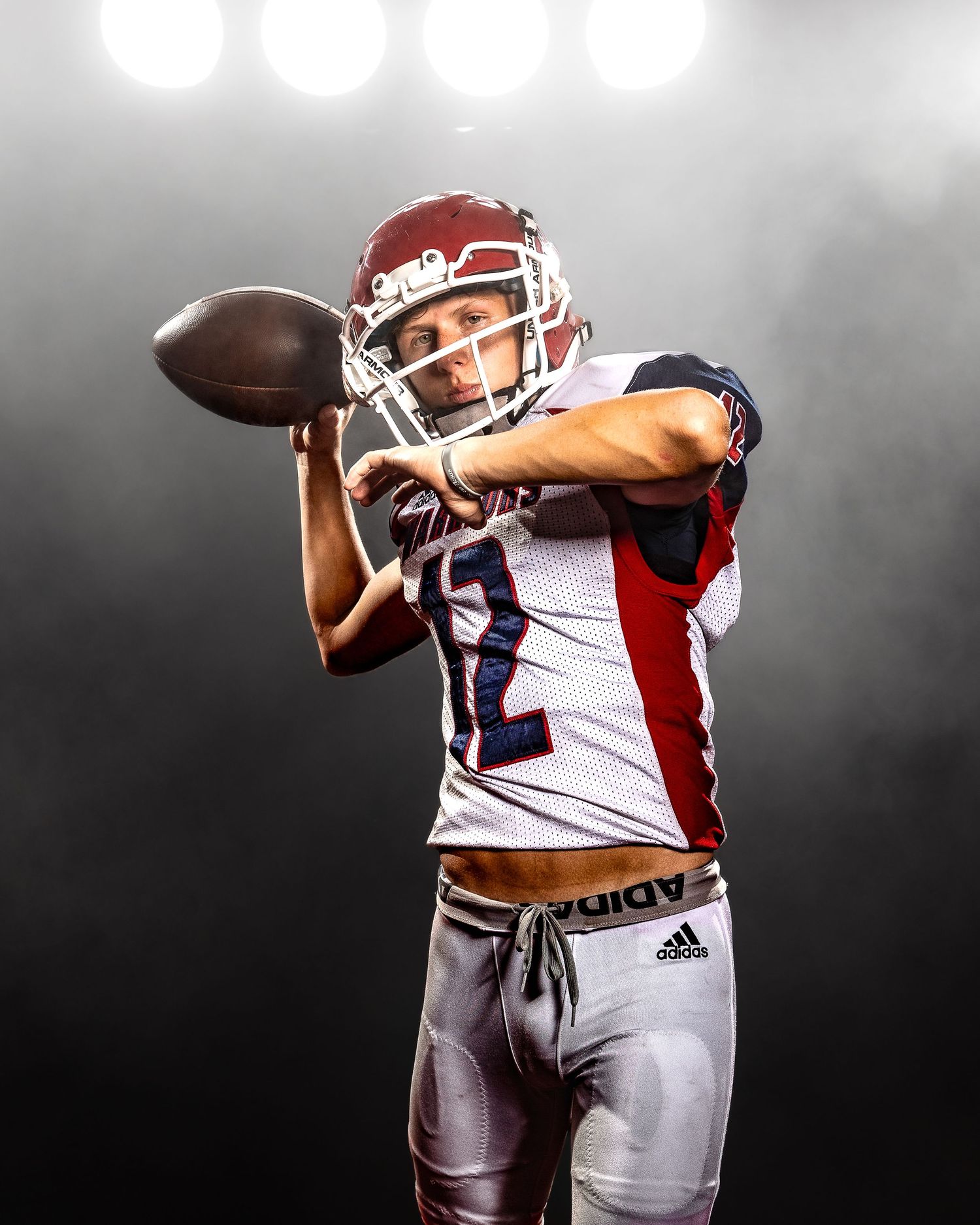 Football player stands on dark field illuminated by stadium lights and stretches during practice session.