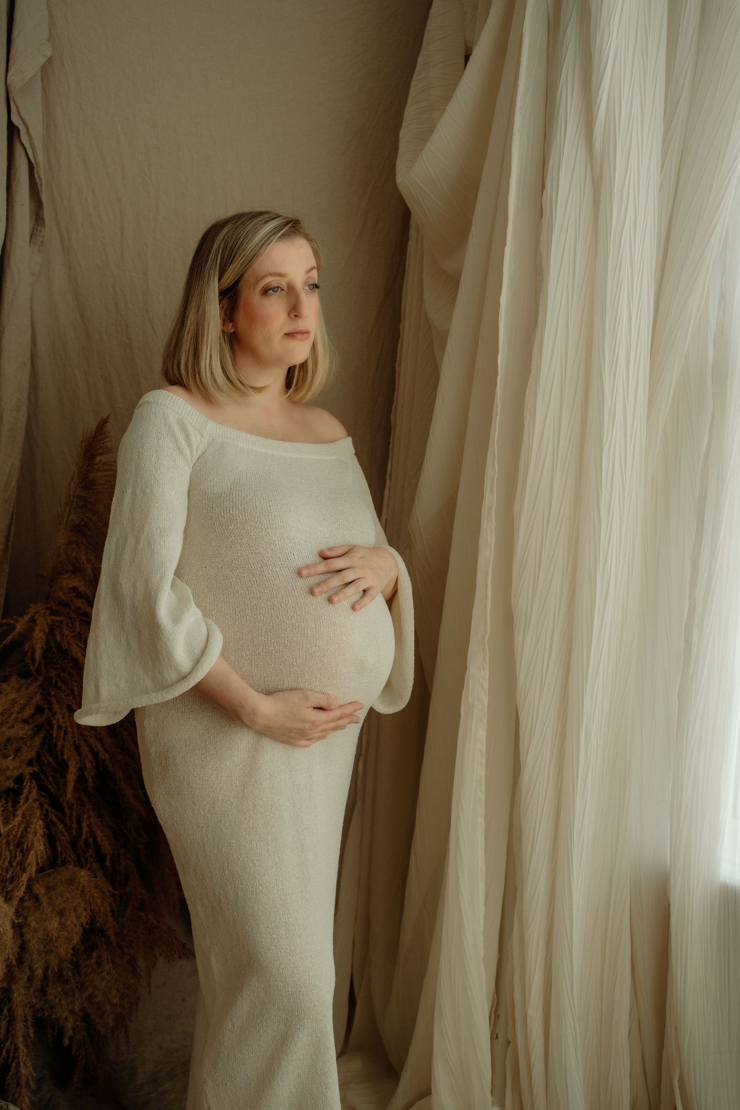 Natural light indoor maternity photoshoot of expecting mother gently holding baby bump