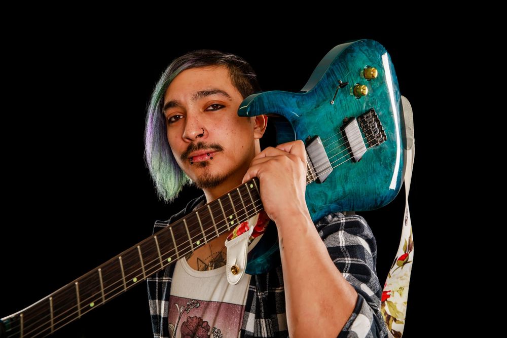 Musician performing with an electric guitar against a dark background with teal lighting effects.