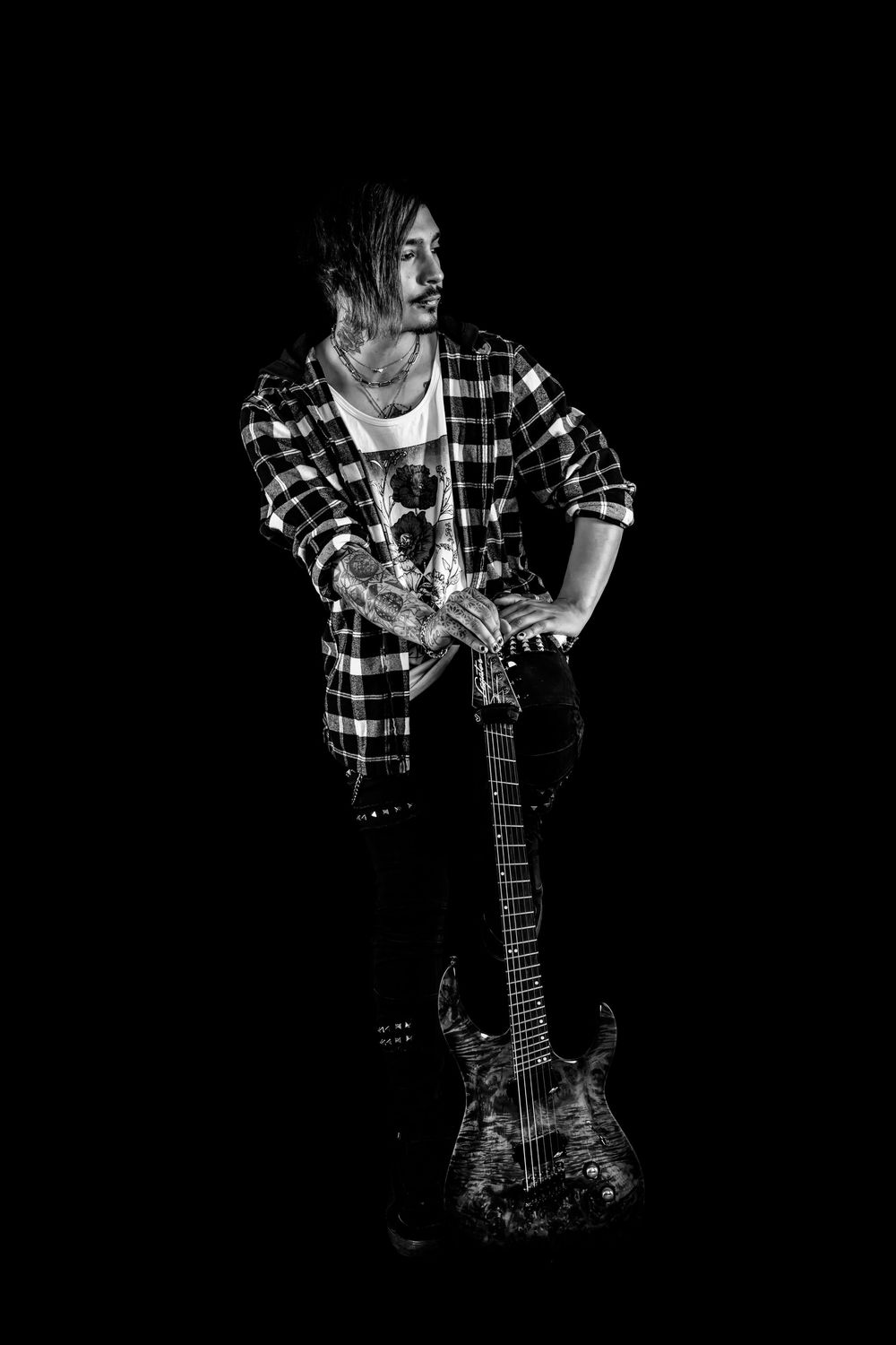 Monochrome portrait of alternative musician holding guitar in casual plaid shirt and jeans.