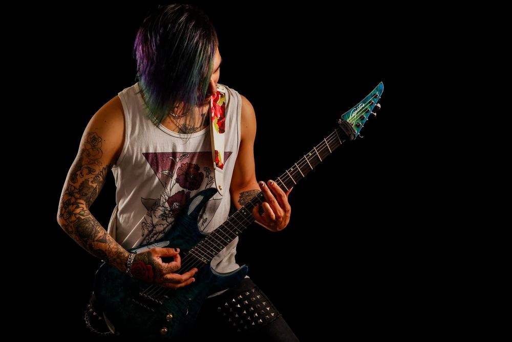 Heavy metal musician playing electric guitar in dramatic low-key lighting with visible tattoos on arm.