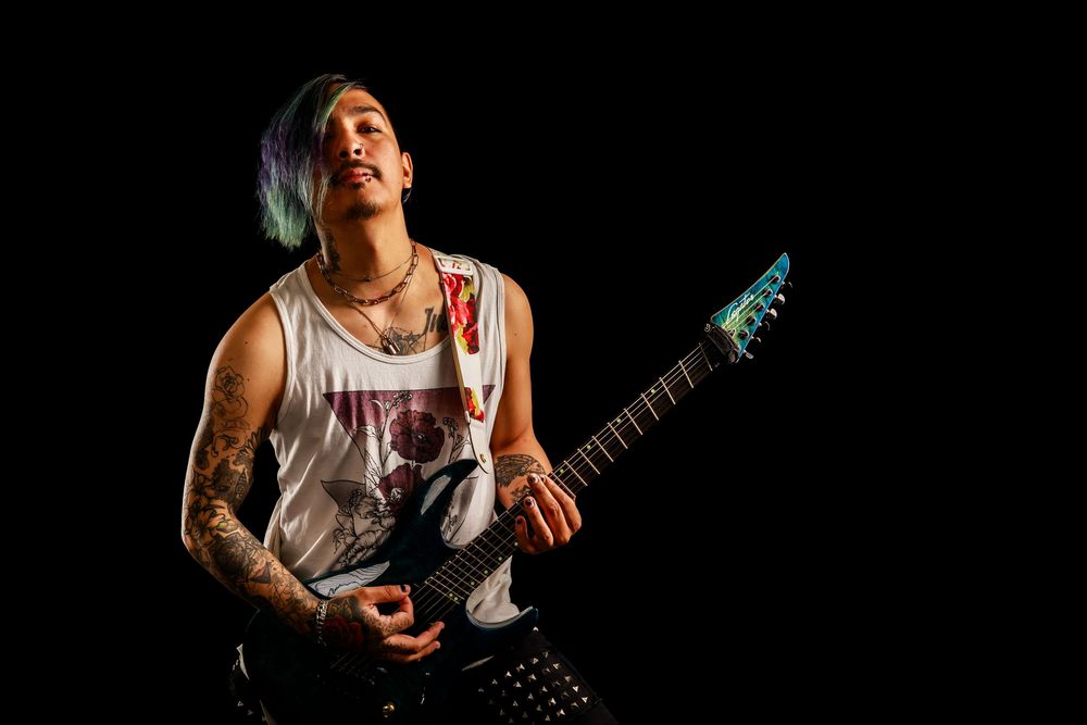 Performer playing guitar in a white tank top on stage with dramatic spotlighting.