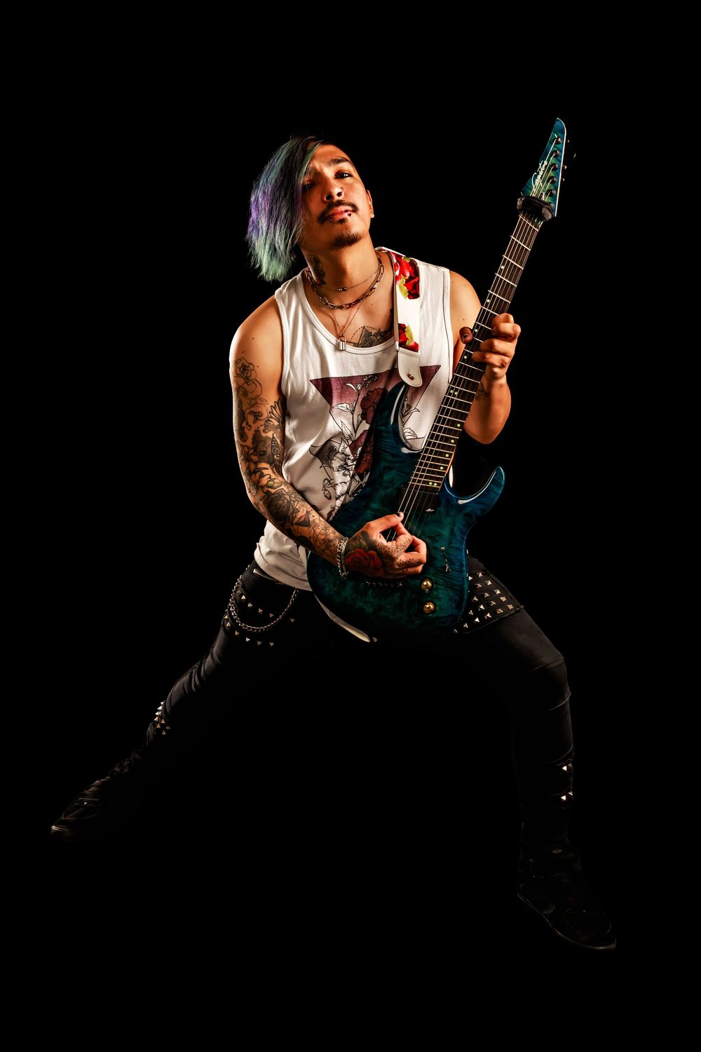 Rock musician with colorful hair performs energetically with electric guitar against black background.