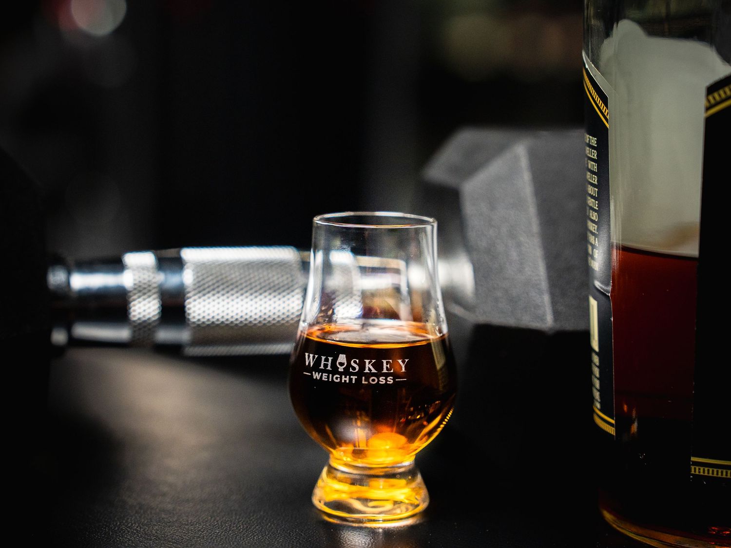 A glencairn glass filled with whiskey sits beside a bottle against a dark background with a micrometer in focus.
