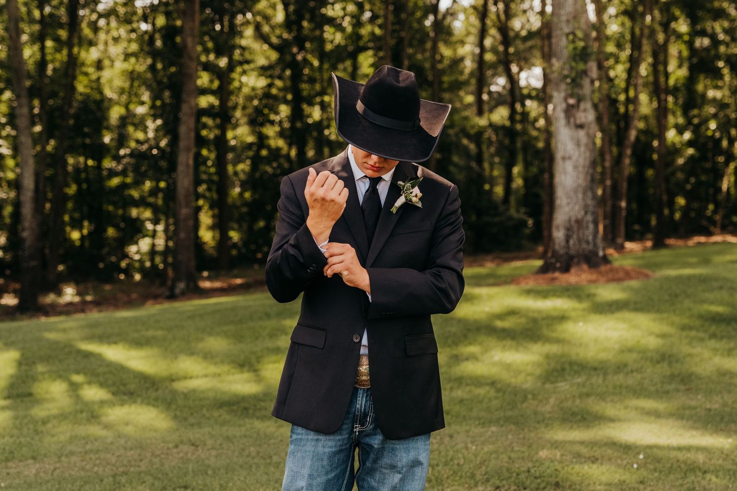 A groom in a black coat and hat adjusting his cufflinks on his wedding day in East Texas.