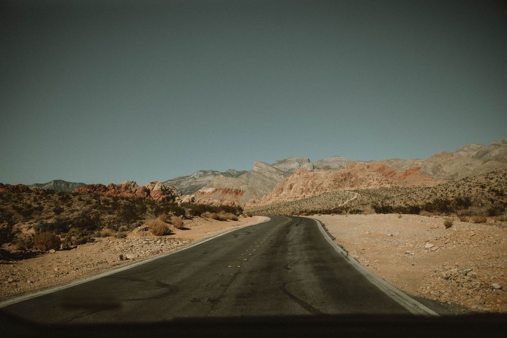 A winding paved road leads through a barren desert landscape with rugged mountains in the background under a moody sky. vegas elopement phot