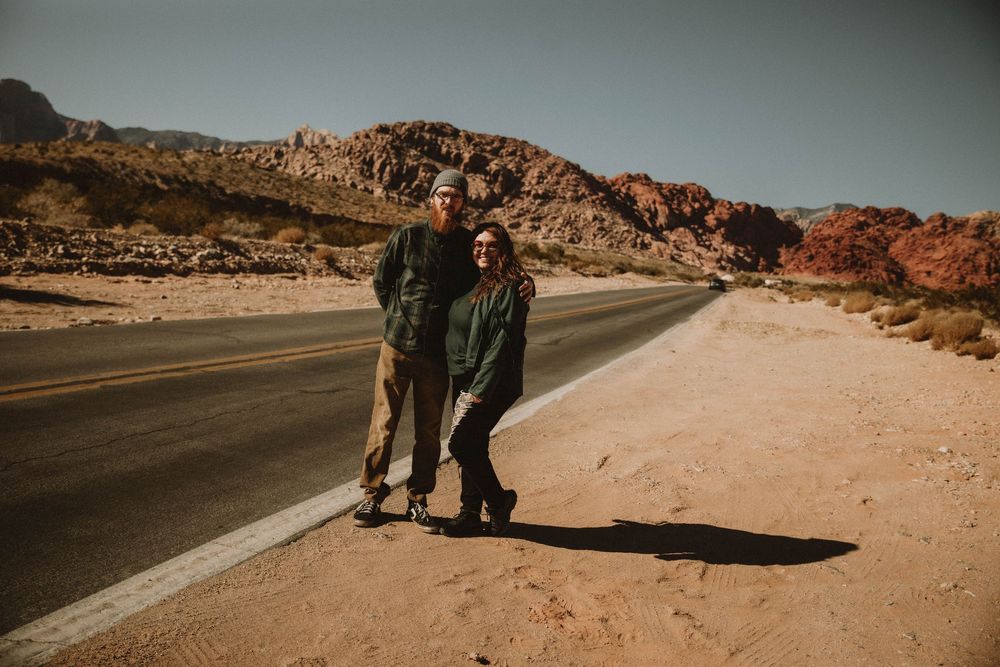 Desert engagement photo session along a winding road with rocky mountains in the background at sunset.