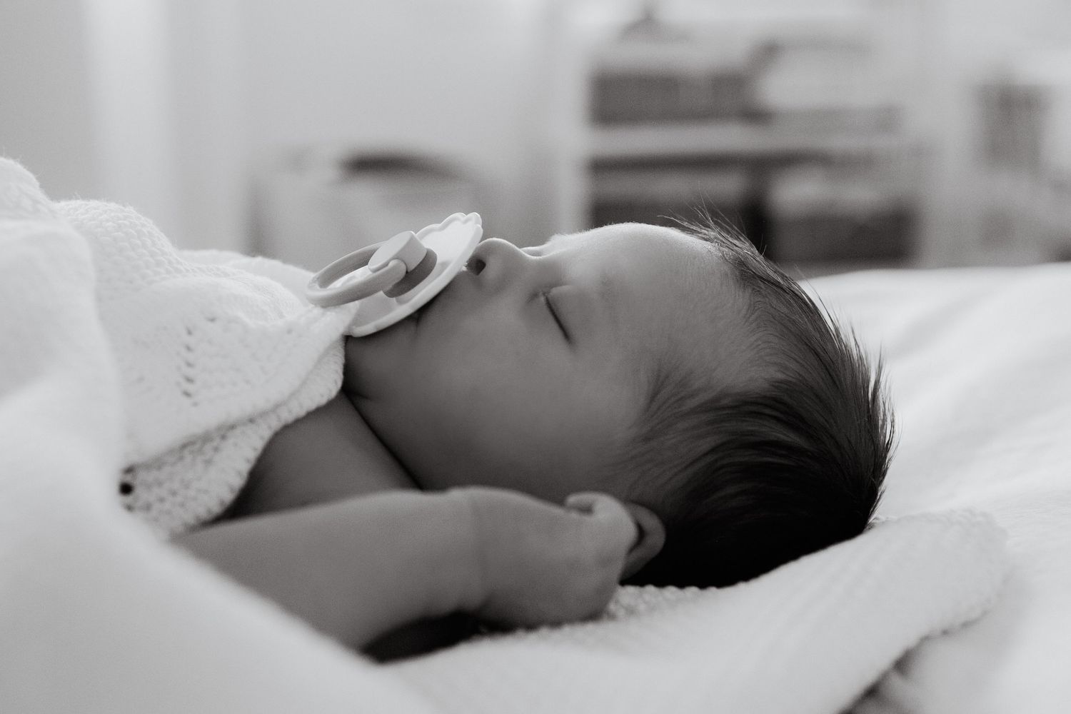 Sleeping newborn baby lying peacefully under white blanket in natural light setting.