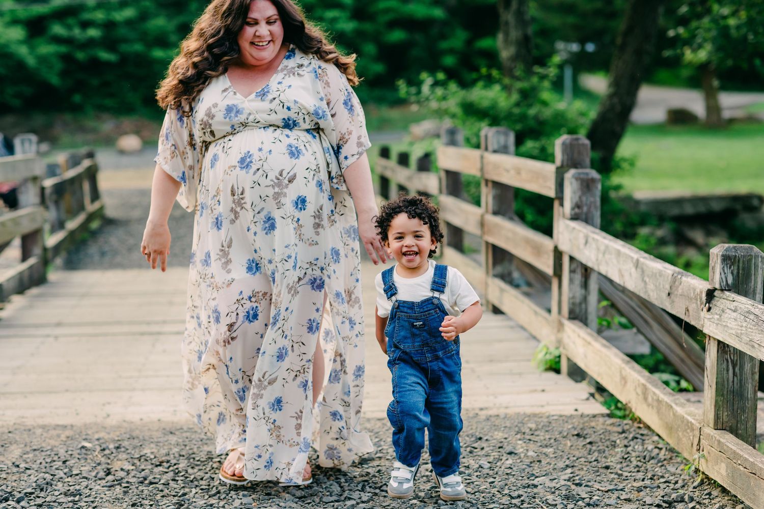 expectant mother in floral dress and toddler in overalls running down the bridge during a maternity shoot at Southford Falls, CT