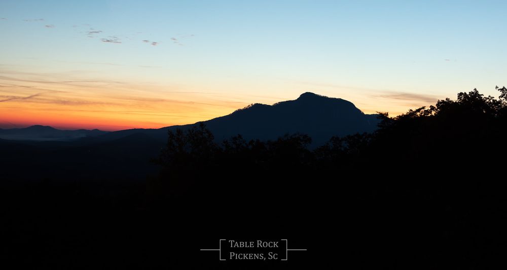 Silhouette of mountain peaks against vibrant orange and blue sunset sky with birds flying overhead.