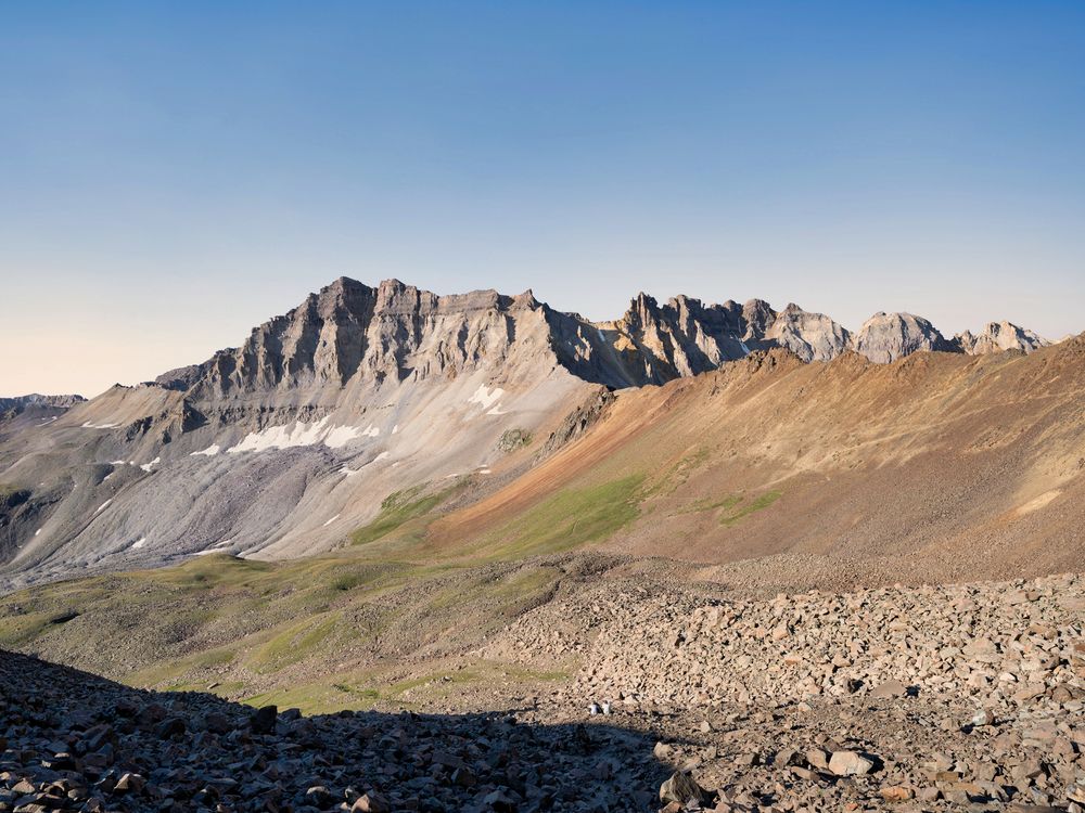 Rocky mountain peaks under a clear blue sky with a green valley and scree slopes in the foreground.