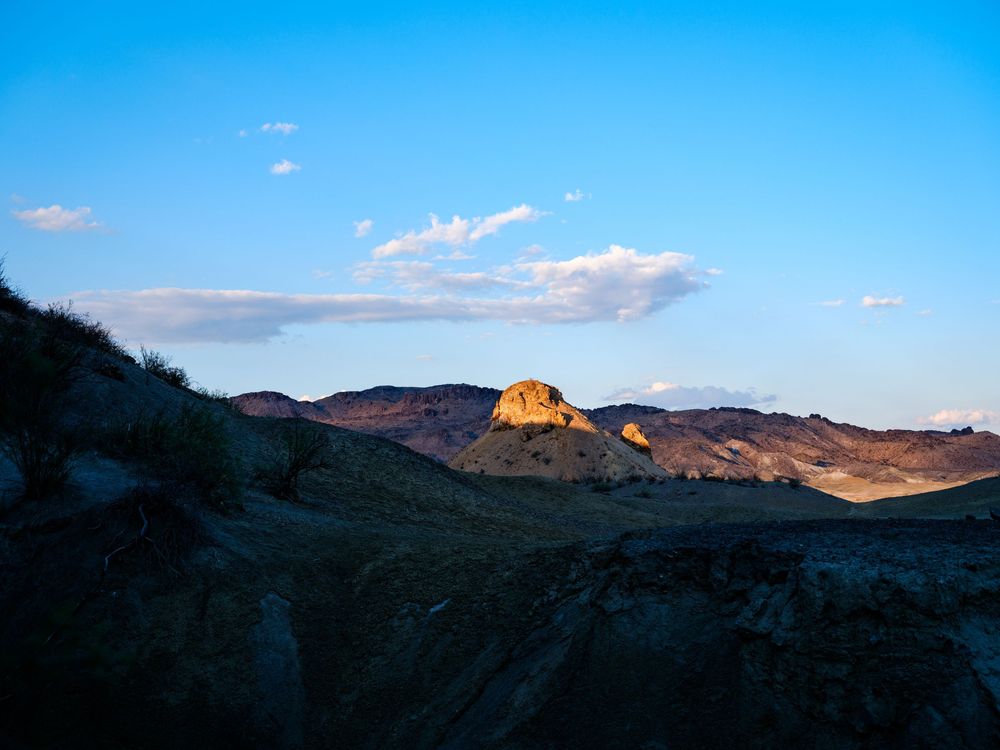Sunlit mountain peaks cast shadows across desert terrain at sunset.