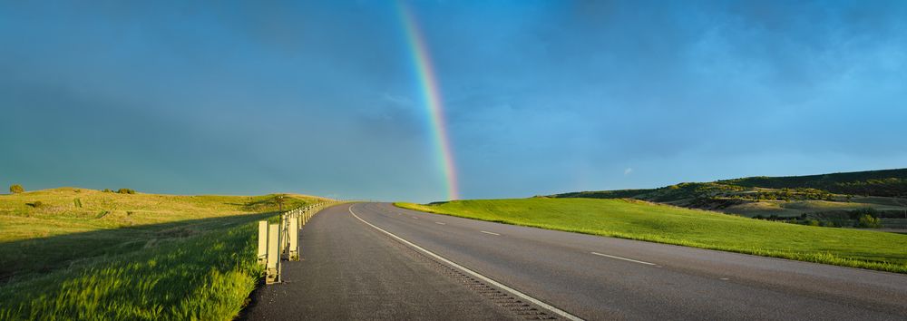 Rainbow arching over rural countryside with green fields and winding road.