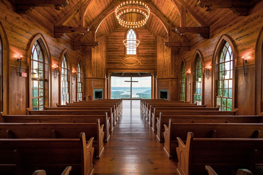 Interior of wooden chapel with arched windows and long rows of empty pews at Top of the Rock in Branson, Missouri