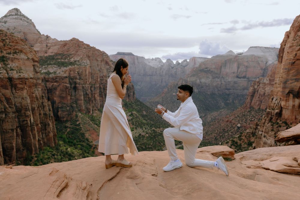 Two people share a special moment on a scenic overlook with dramatic red rock cliffs and canyons of Zion National Park.