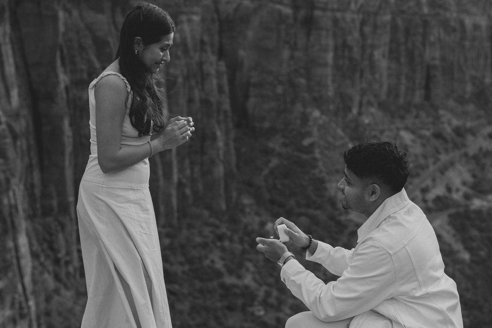 A couple shares a romantic moment during a marriage proposal in a wooded outdoor setting.