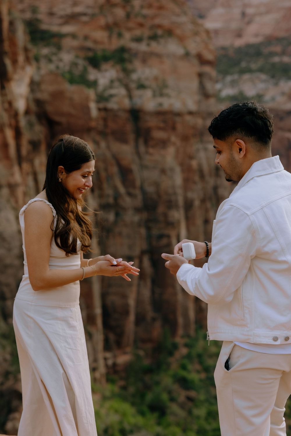 A couple in white outfits standing together against a rocky cliff wall creating a romantic engagement photo sequence.