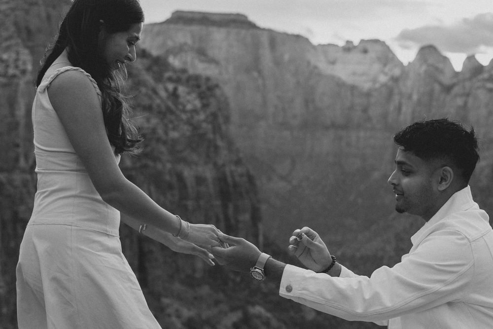 A romantic proposal moment between two people atop scenic mountain cliffs at Zion National Park during sunset.