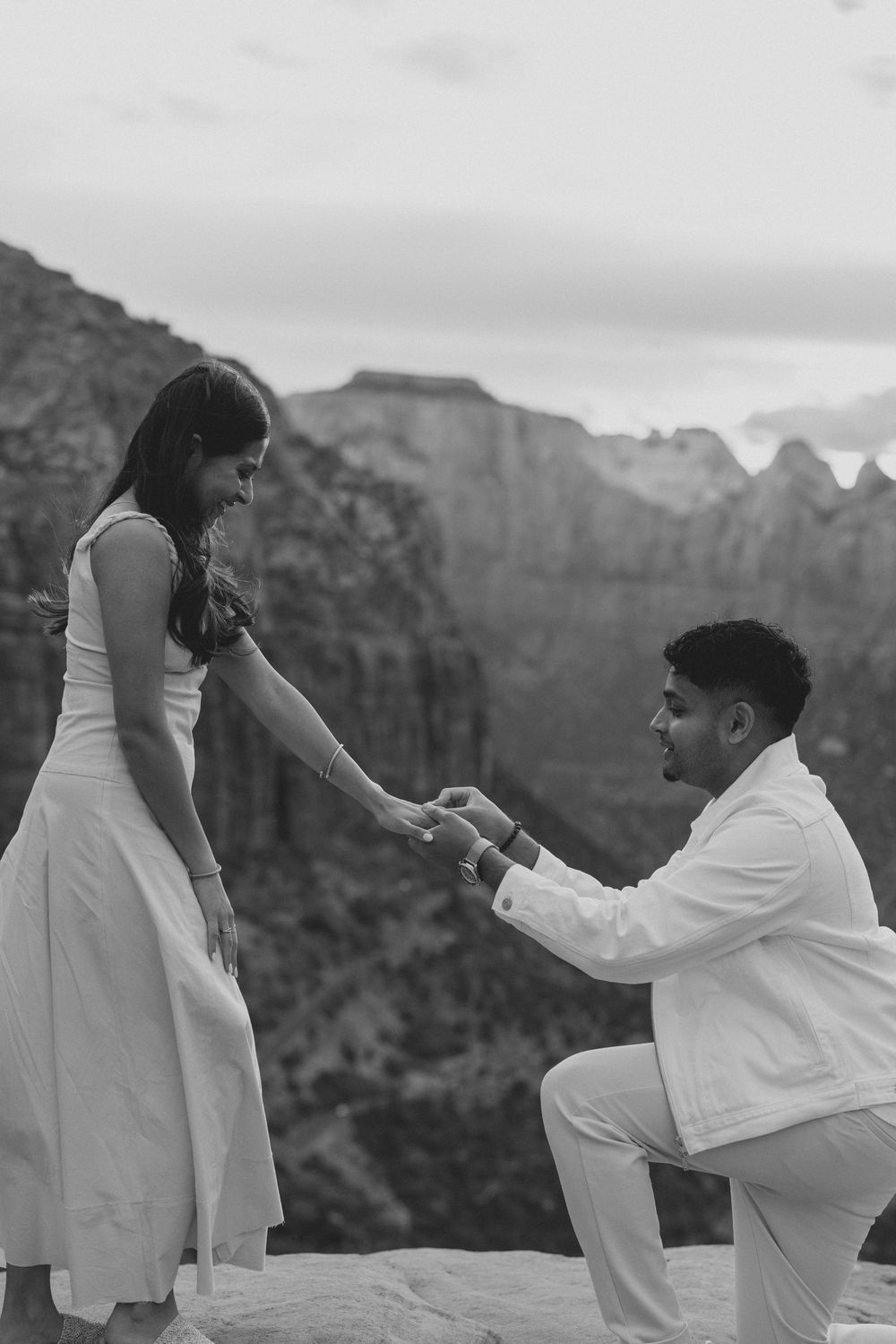 A black and white capture of a proposal moment on a cliff edge with majestic canyon walls in the background.