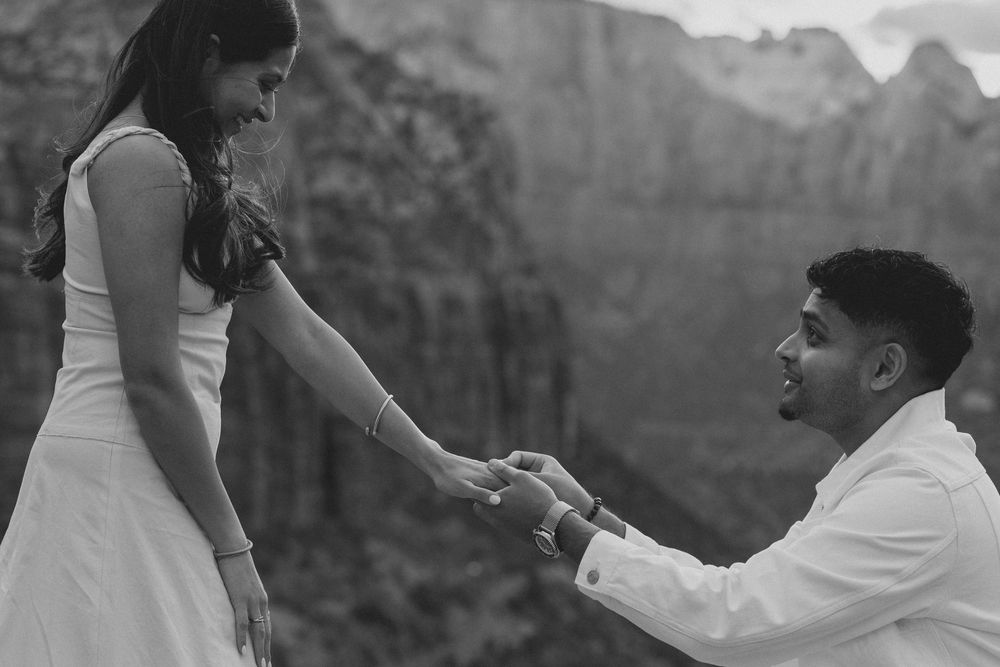 A romantic marriage proposal scene against a dramatic mountain backdrop at sunset.
