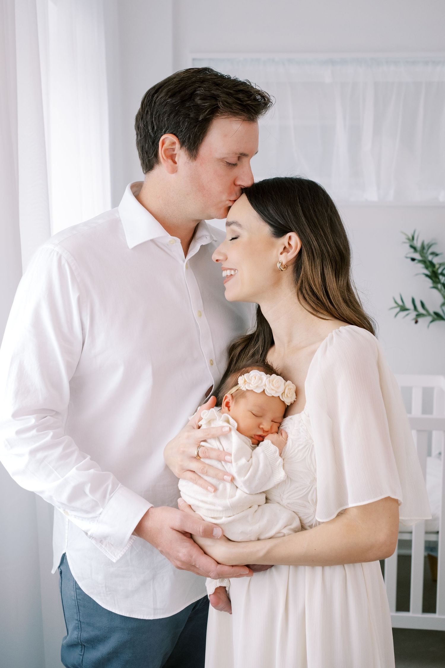 Mother in white lace hugging small baby in grey onesie against neutral background in a series of emotional portraits.