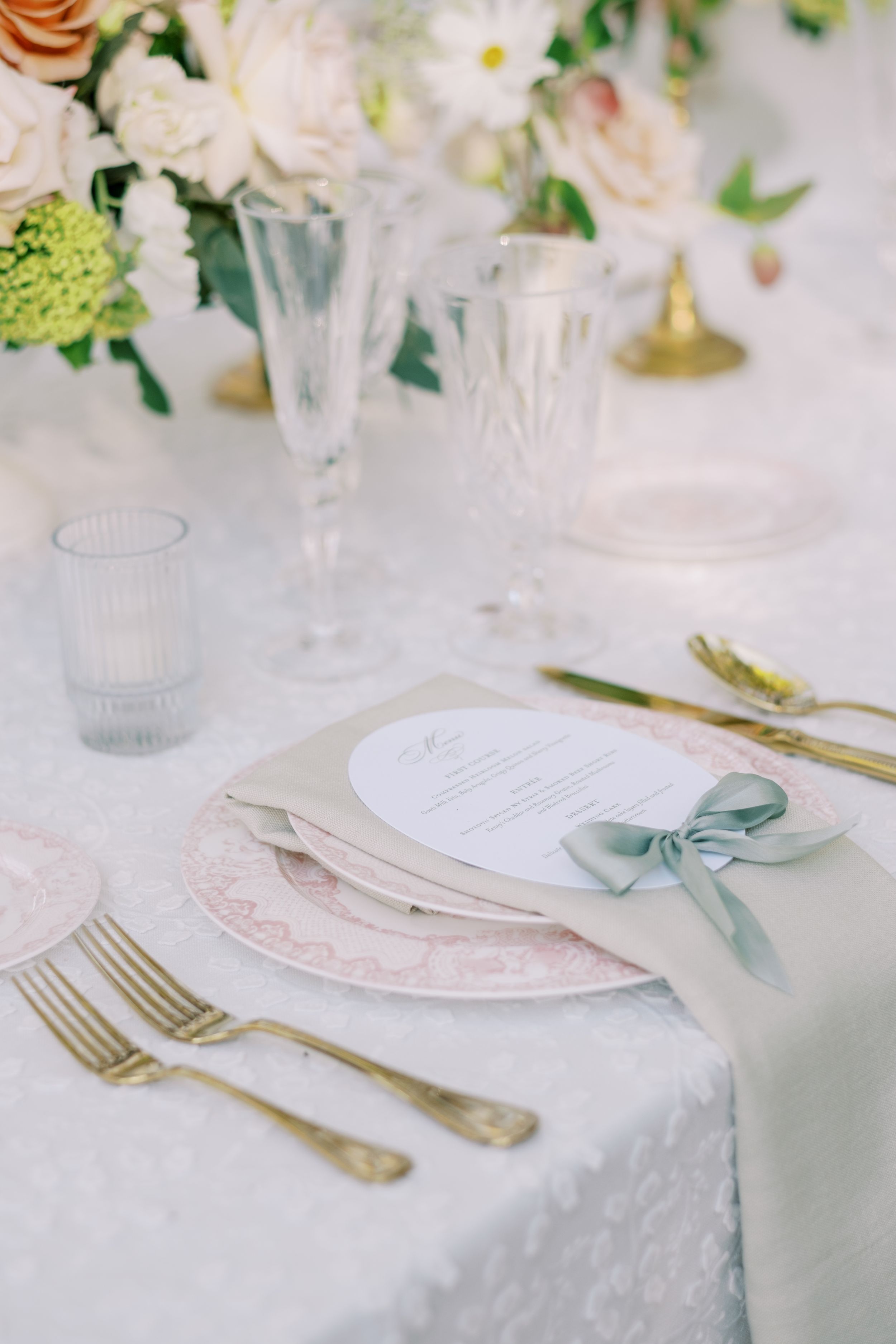 Elegant wedding table setting with soft white linens, floral arrangements, and delicate blue ribbon accents on place cards.