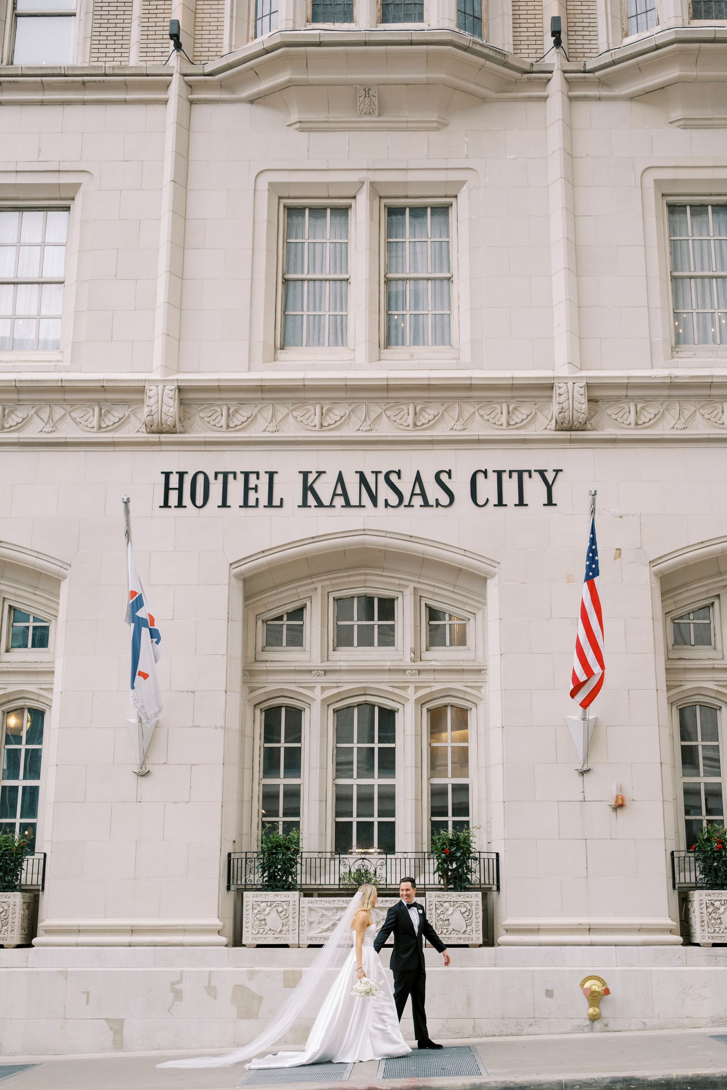 Elegant bride and groom pose outside the historic Hotel Kansas City building with its grand white facade.