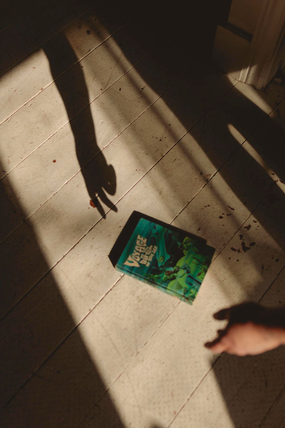 Shadow play as the sun rises, sending side light through the window of a bookshop. A hand reaches for the book, drawing a shadow on floor.