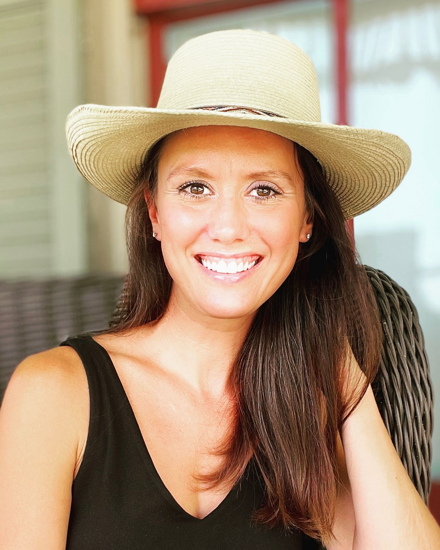 Woman in a straw hat and black top sitting on a porch.