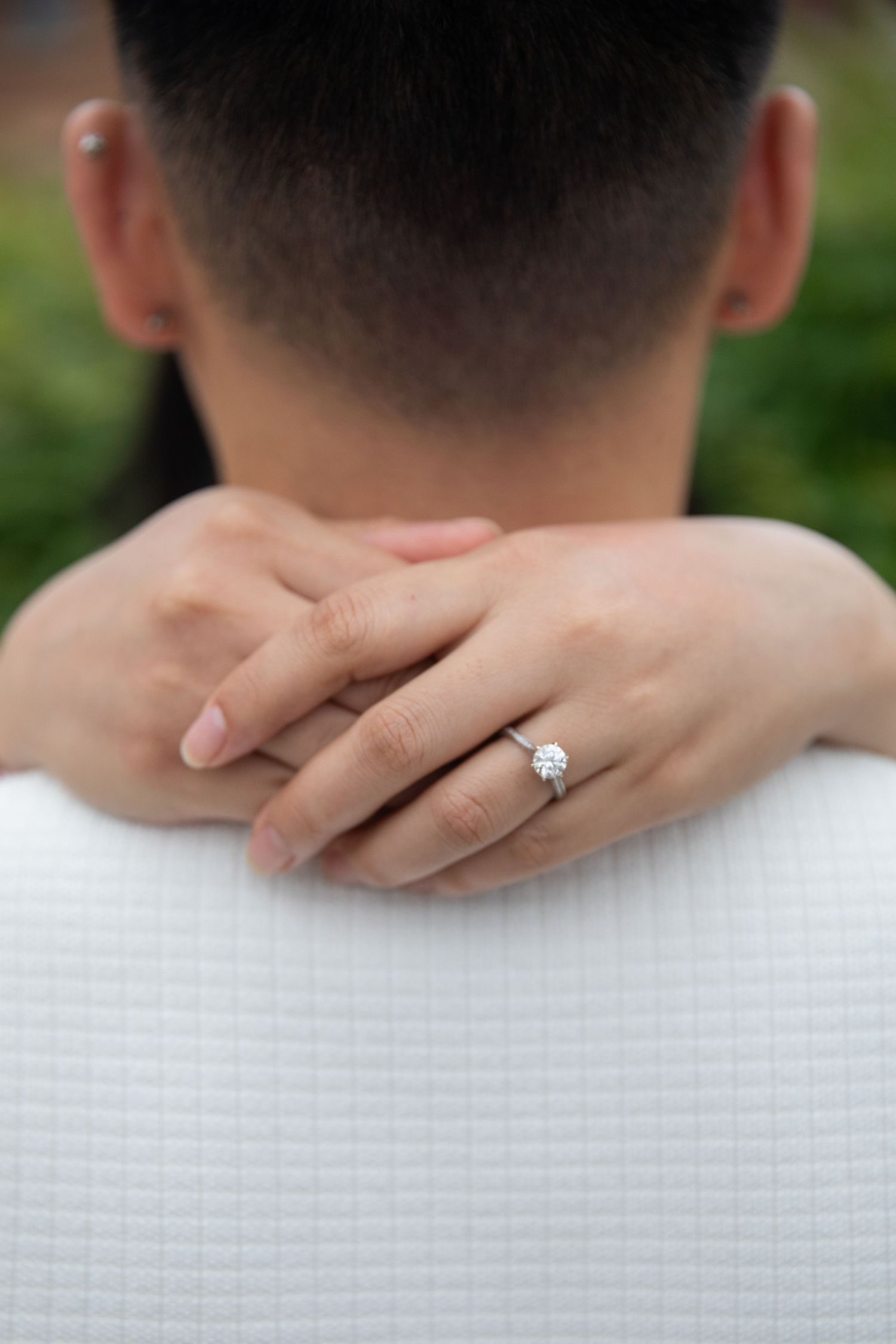 Woman's hand with sparkling engagement ring embraces someone wearing a white shirt from behind.