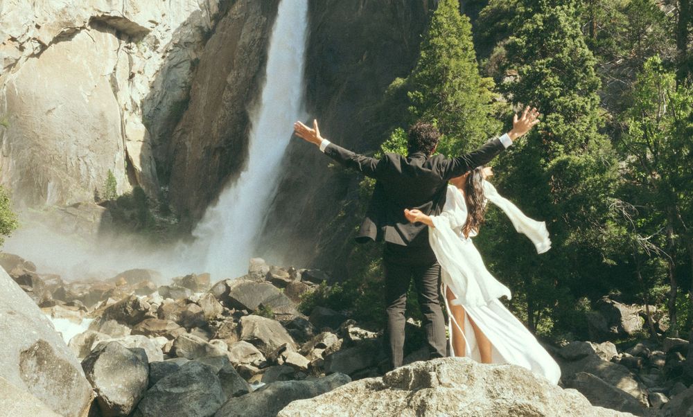 A scenic waterfall cascades down rocky cliffs surrounded by lush green forest in a beautiful natural setting.