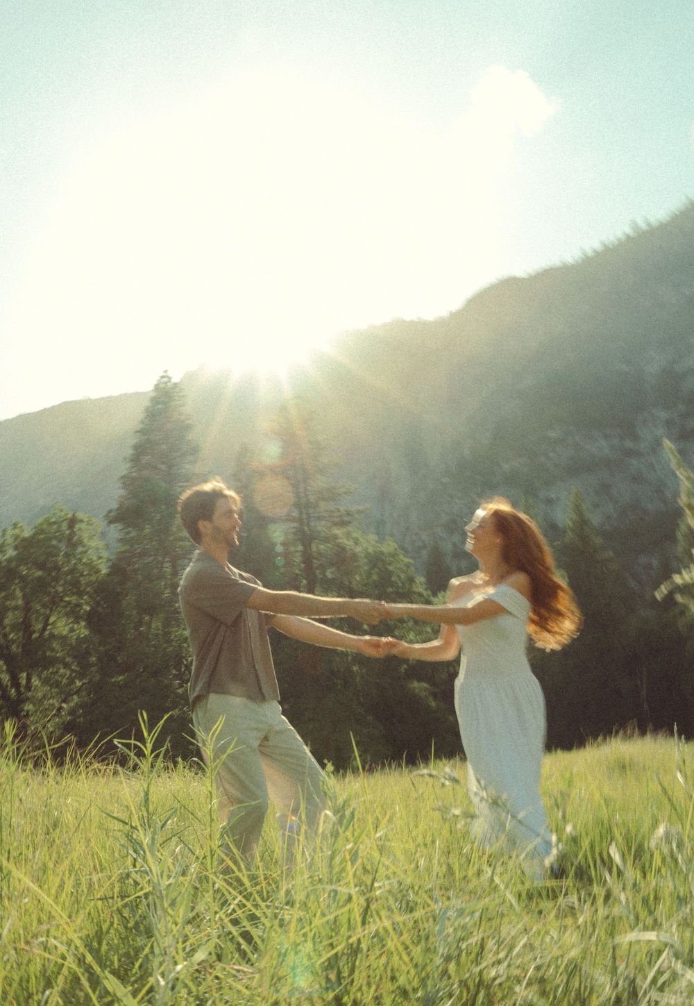 A couple spins together in a sunny mountain meadow on a bright summer day, creating a romantic moment in nature.