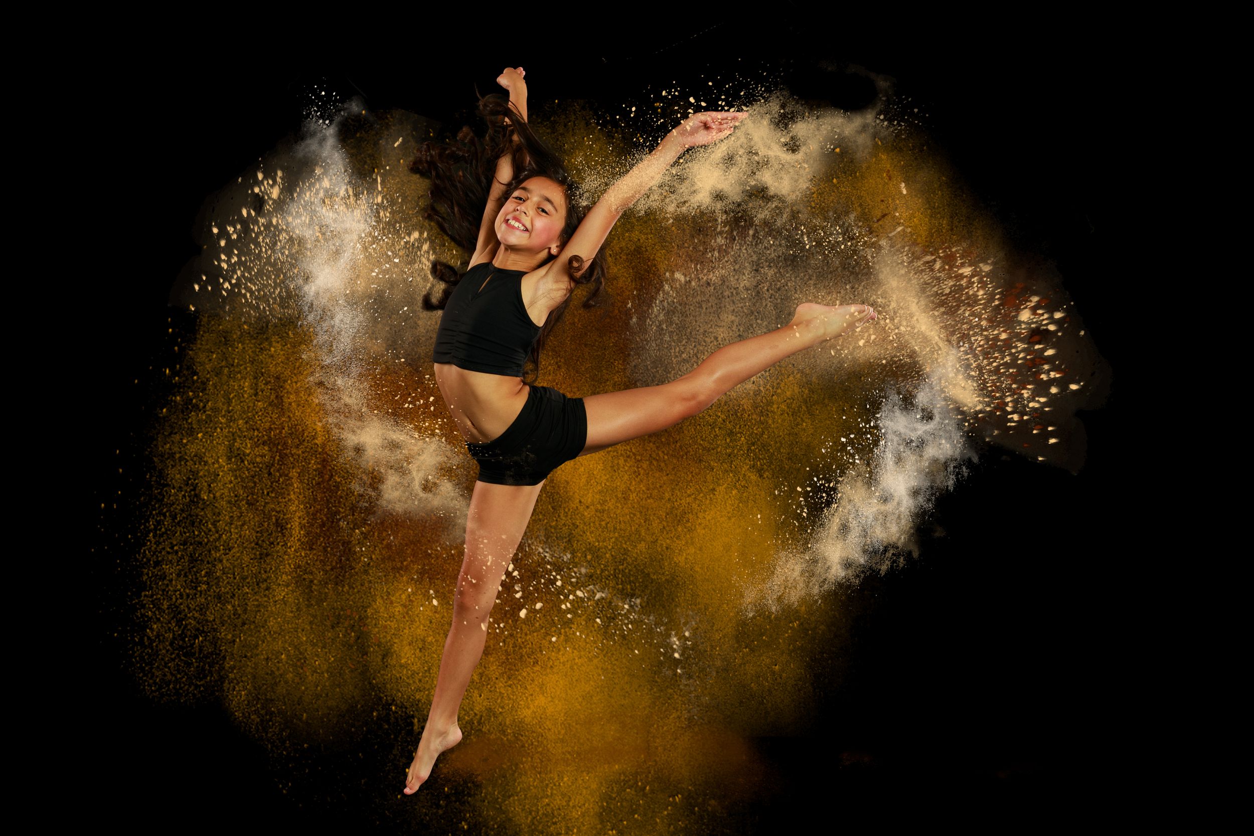 Dancer creating dynamic movement with gold powder effects against black background.