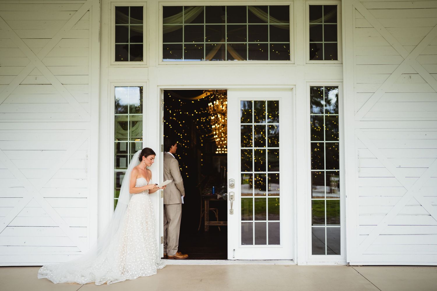 An elegant rustic-style white barn venue with French doors and windows glows warmly in natural daylight.
