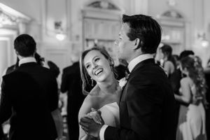 A couple shares a joyful laugh while dancing together at an elegant wedding reception in black and white.