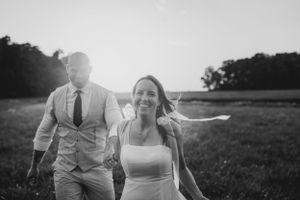 A couple joyfully walks through a sunlit meadow in black and white wedding attire.
