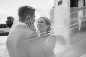Black and white romantic wedding moment captured through soft veil at outdoor venue.