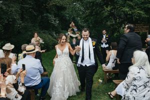 Outdoor wedding ceremony in a lush garden setting with guests seated on wooden benches surrounded by greenery.