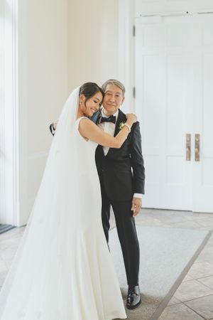 A tender moment between a bride in a white gown and an older person in a black tuxedo at a wedding celebration.