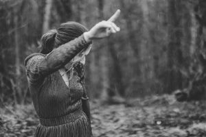 A person in a sweater pointing upward while standing in a misty forest, captured in black and white photography.
