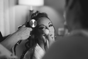 Black and white photo showing someone getting makeup professionally applied while having their hair styled.