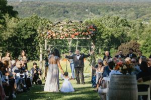 Outdoor wedding ceremony with floral arch and wine barrel set against rolling hills and green landscape backdrop.